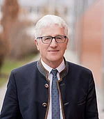 Ein freundlich lächelnder Herr mit Brille und silbergrauen Haaren.