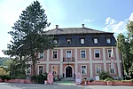 Auf dem Foto ist das Schloss Teublitz zu sehen, ein zweigeschossiger historischer Bau mit hellem Mauerwerk und Mansarddach, der von Bäumen und Grünflächen des Schlossparks umgeben ist und zu den bedeutenden Kulturdenkmälern der Stadt gehört.
