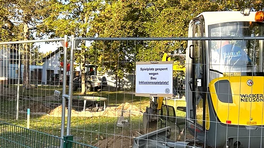 Ein abgesperrter Spielplatz mit Bauzaun, Bagger und Erdarbeiten zeigt den Beginn der Bauarbeiten für den neuen Inklusionsspielplatz.