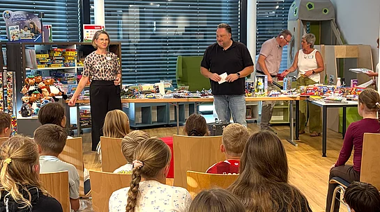 Zahlreiche Kinder sitzen in der neuen Stadtbücherei vor Büchereileiterin Corinna Höfler und Bürgermeister Thomas Beer, die gemeinsam durch die Preisverleihung des Sommerferien-Leseclubs führen.