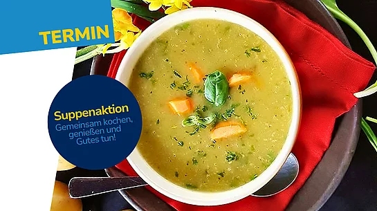 Eine weiße Schüssel mit cremiger Gemüsesuppe, garniert mit Karottenstückchen und frischen Kräutern. Die Schüssel steht auf einer roten Stoffserviette und einem dunklen Teller. Rundherum liegen Kartoffeln, grüne Blätter und gelbe Blüten auf einem schwarzen Untergrund.