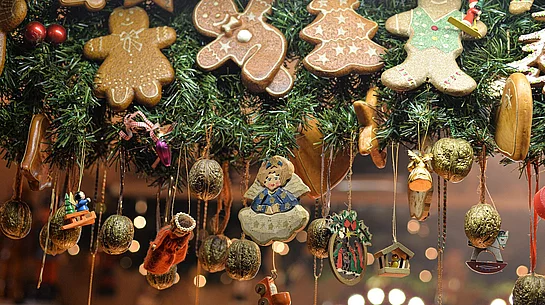 Das Foto zeigt eine festlich geschmückte Girlande mit Lebkuchenfiguren, kleinen Holzornamenten und goldenen Nüssen. Im Hintergrund sorgen warme Lichter für eine gemütliche, weihnachtliche Atmosphäre.