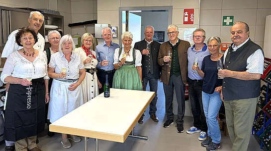 Die Mitglieder des Seniorenbeirats stehen vor Beginn des Oktoberfests gemeinsam in der Küche des Mehrgenerationenhauses und halten zum Teil Gläser zum Anstoßen in den Händen.