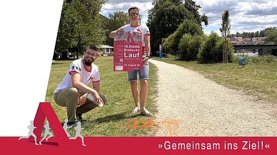 Eine Werbegrafik zeigt zwei Personen in Laufshirts des Städtedreieckslaufs an einem geschotterten Uferweg. Eine Person kniet neben einer orangefarbenen Streckenmarkierung auf dem Boden, die andere hält das Veranstaltungsplakat des 16. Städtedreieckslaufs in die Kamera. Im Hintergrund sind Bäume, die Naab sowie eine Brücke zu sehen. Am unteren Bildrand steht der Slogan „Gemeinsam ins Ziel!“. Die Grafik weist darauf hin, dass die Laufstrecken bereits markiert sind und zum Training genutzt werden können.