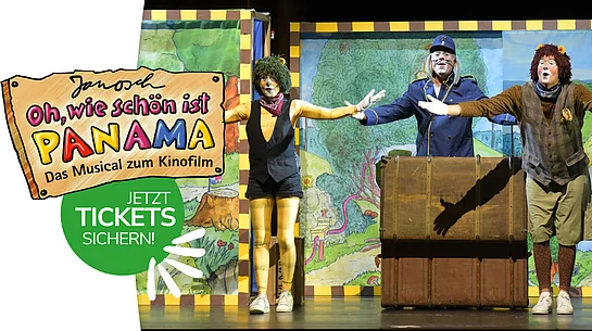 Auf dem Bild stehen drei verkleidete Schauspielerinnen und Schauspieler auf einer bunten Theaterbühne, breiten die Arme aus und spielen vor gemalten Kulissen eine fröhliche Szene aus dem Musical „Oh, wie schön ist Panama“.