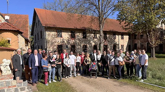 Eine große Gruppe von Menschen steht bei sonnigem Wetter vor einem historischen Gebäude und posiert gemeinsam für ein Foto.