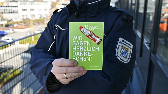 Auf dem Bild hält eine uniformierte Person eine grüne Karte mit der Aufschrift „Wir sagen herzlich Dankeschön!“ sowie einem kleinen Schoko-Nikolaus darauf gut sichtbar in die Kamera.